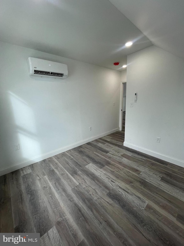 spare room featuring dark wood-type flooring, a wall unit AC, and vaulted ceiling