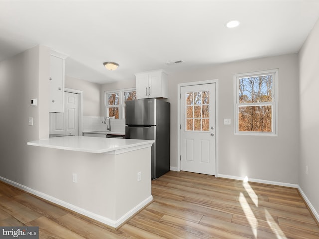 kitchen with sink, white cabinets, kitchen peninsula, backsplash, and stainless steel fridge