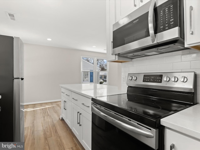 kitchen featuring backsplash, white cabinets, appliances with stainless steel finishes, and light hardwood / wood-style flooring