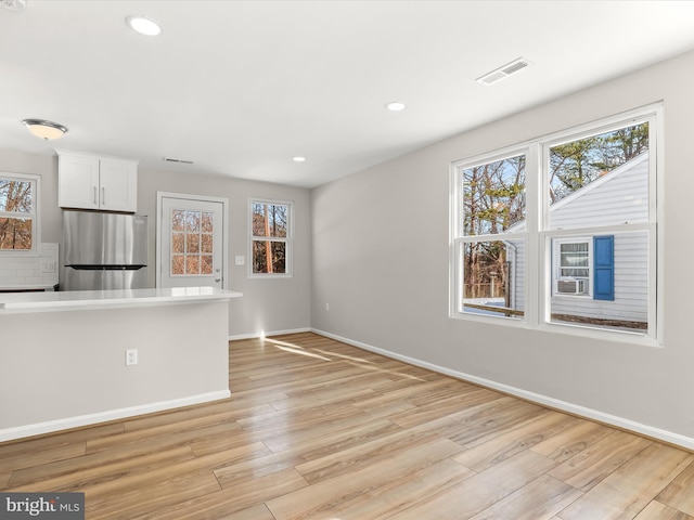 kitchen featuring light hardwood / wood-style floors, stainless steel fridge, white cabinetry, and backsplash