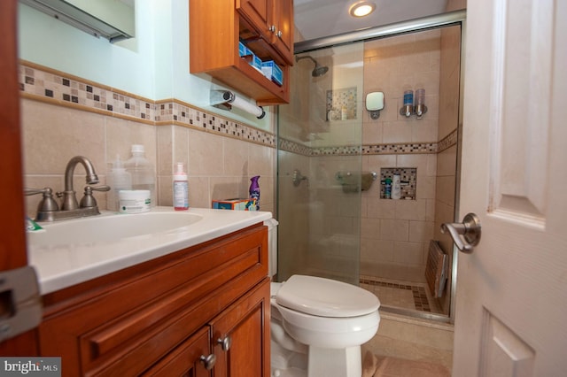 bathroom with tile walls, toilet, a shower with door, and vanity