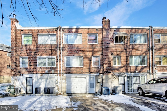 snow covered back of property featuring central AC unit and a garage