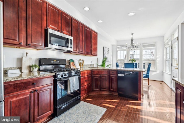 kitchen featuring sink, dark wood-type flooring, light stone counters, black appliances, and decorative light fixtures