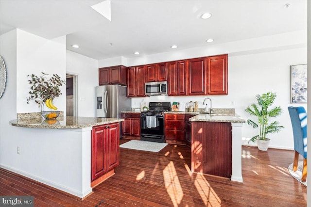 kitchen with stainless steel appliances, dark hardwood / wood-style flooring, light stone countertops, and kitchen peninsula