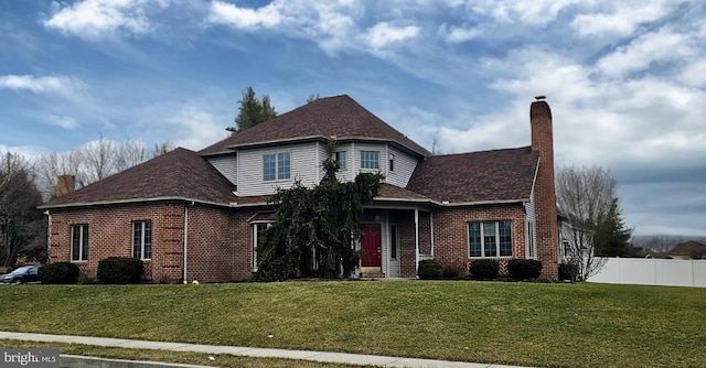 view of front of home featuring brick siding, fence, a chimney, and a front lawn