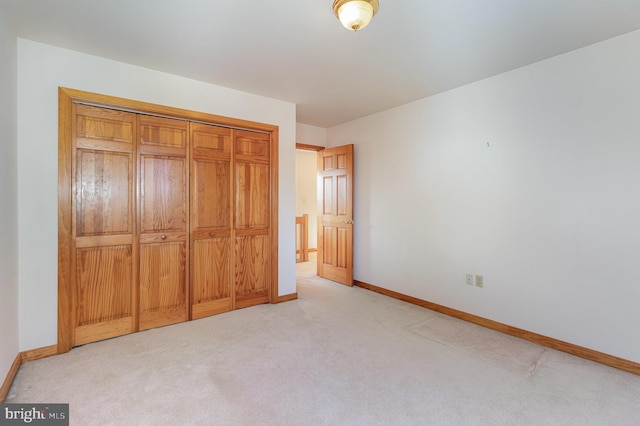 unfurnished bedroom with a closet, light colored carpet, and baseboards