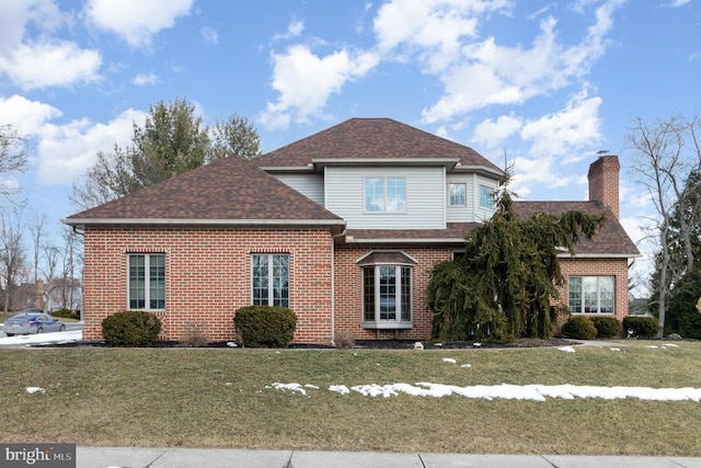 view of front of house with a front yard, brick siding, a chimney, and roof with shingles