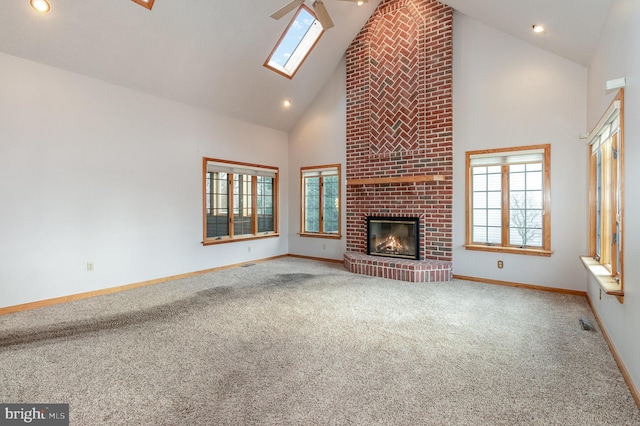 unfurnished living room with a skylight, a fireplace, carpet flooring, high vaulted ceiling, and baseboards