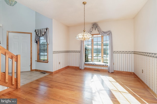 unfurnished dining area featuring wainscoting, an inviting chandelier, and wood finished floors