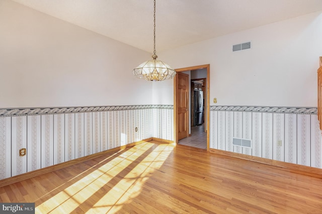 spare room featuring a wainscoted wall, visible vents, a chandelier, and wood finished floors