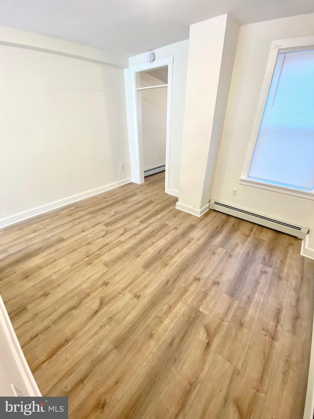 unfurnished bedroom featuring light hardwood / wood-style floors and a baseboard heating unit