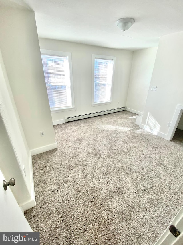 carpeted spare room featuring a healthy amount of sunlight and a baseboard heating unit