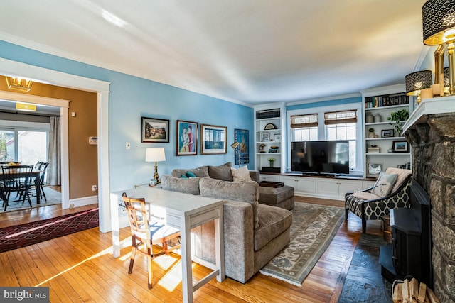 living room with crown molding, built in shelves, a fireplace, and hardwood / wood-style flooring