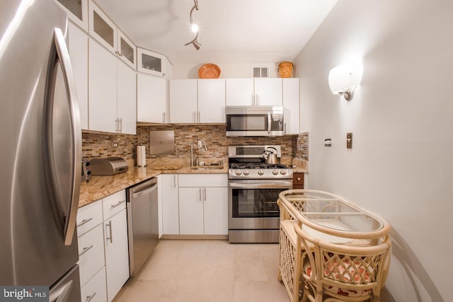 kitchen featuring appliances with stainless steel finishes, light stone countertops, decorative backsplash, white cabinets, and sink