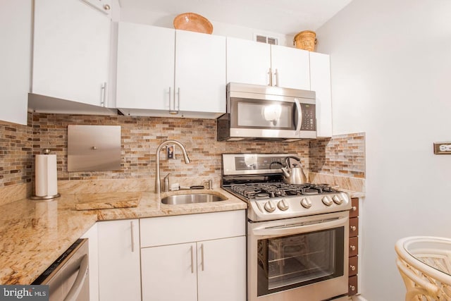 kitchen featuring stainless steel appliances, sink, white cabinets, decorative backsplash, and light stone countertops