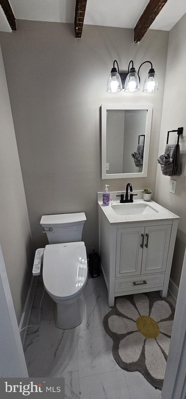 bathroom with toilet, vanity, and beam ceiling