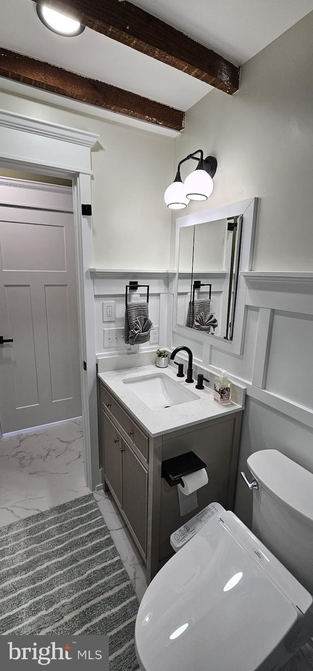 bathroom with beamed ceiling, vanity, and toilet