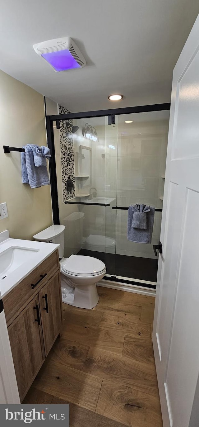 bathroom featuring vanity, toilet, a shower with shower door, and hardwood / wood-style floors