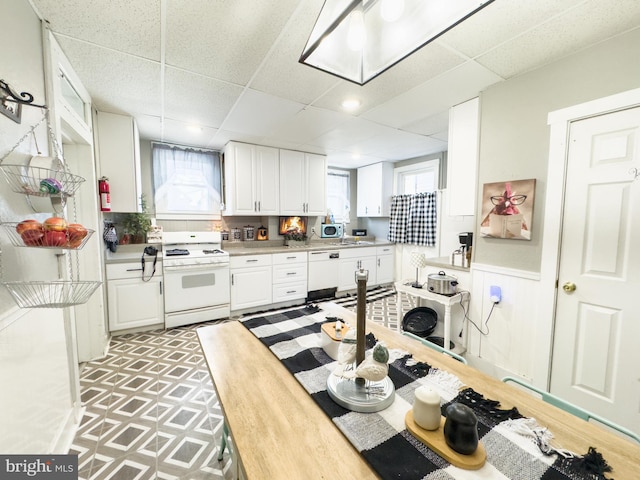 kitchen featuring a paneled ceiling, white cabinetry, sink, and white appliances