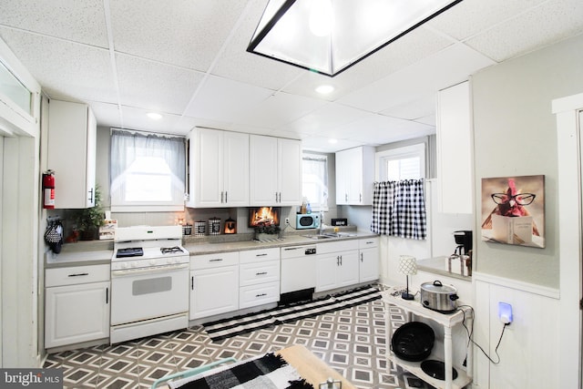 kitchen featuring plenty of natural light, white appliances, a paneled ceiling, white cabinets, and sink