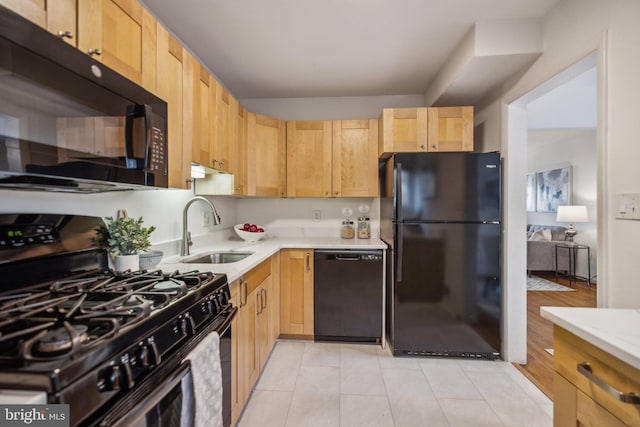 kitchen with light brown cabinetry, sink, light tile patterned floors, light stone counters, and black appliances