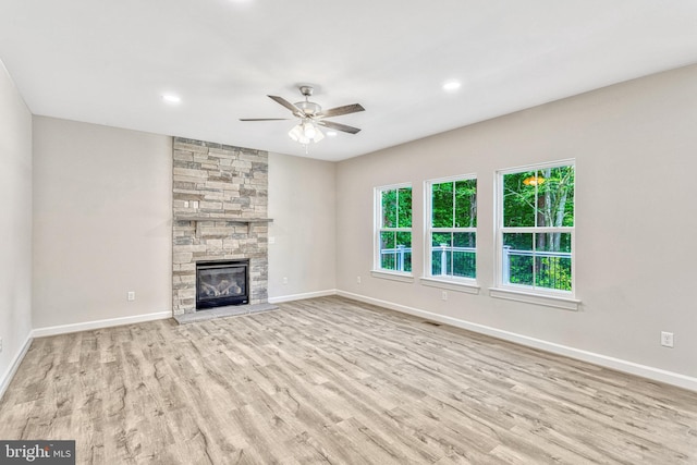 unfurnished living room featuring ceiling fan, a stone fireplace, and light hardwood / wood-style flooring