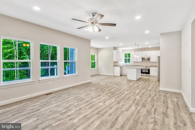 unfurnished living room with light wood-type flooring, ceiling fan, and a healthy amount of sunlight