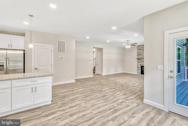 kitchen featuring ceiling fan, a fireplace, pendant lighting, stainless steel refrigerator with ice dispenser, and white cabinets