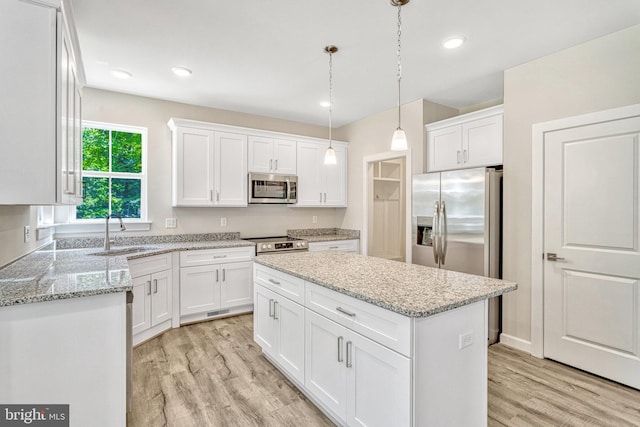 kitchen with white cabinets, a kitchen island, stainless steel appliances, sink, and hanging light fixtures