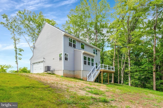 back of property with a garage, a wooden deck, a lawn, and central air condition unit