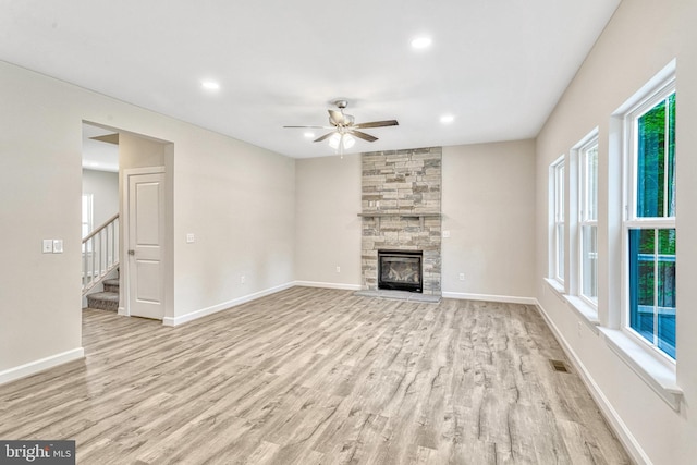 unfurnished living room featuring ceiling fan, a wealth of natural light, light hardwood / wood-style flooring, and a stone fireplace