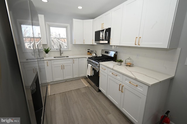 kitchen featuring light stone countertops, sink, light hardwood / wood-style floors, white cabinetry, and stainless steel range with gas stovetop