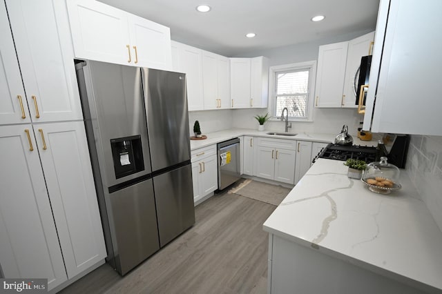 kitchen with white cabinets, sink, appliances with stainless steel finishes, light hardwood / wood-style floors, and light stone counters