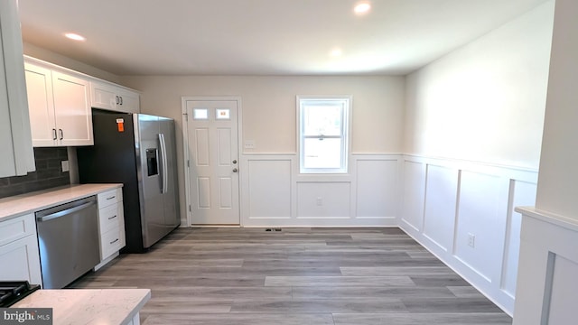 kitchen featuring appliances with stainless steel finishes, light hardwood / wood-style floors, white cabinetry, and tasteful backsplash