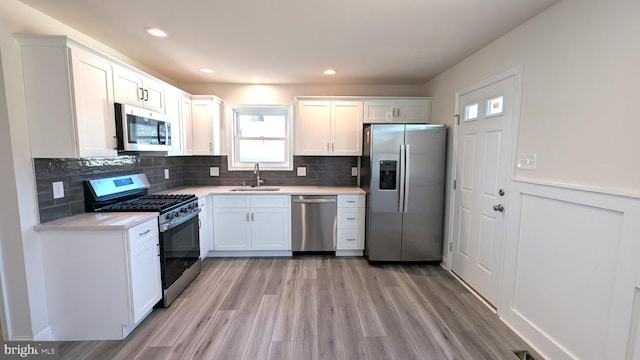 kitchen with sink, stainless steel appliances, light hardwood / wood-style floors, decorative backsplash, and white cabinets