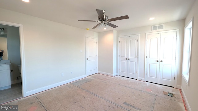 unfurnished bedroom with ceiling fan, ensuite bathroom, and two closets