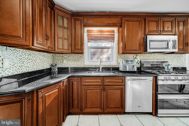 kitchen featuring sink, backsplash, dark stone countertops, light tile patterned flooring, and appliances with stainless steel finishes