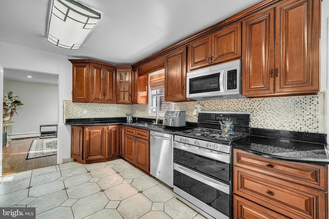 kitchen with dark stone counters, sink, stainless steel appliances, and a baseboard heating unit