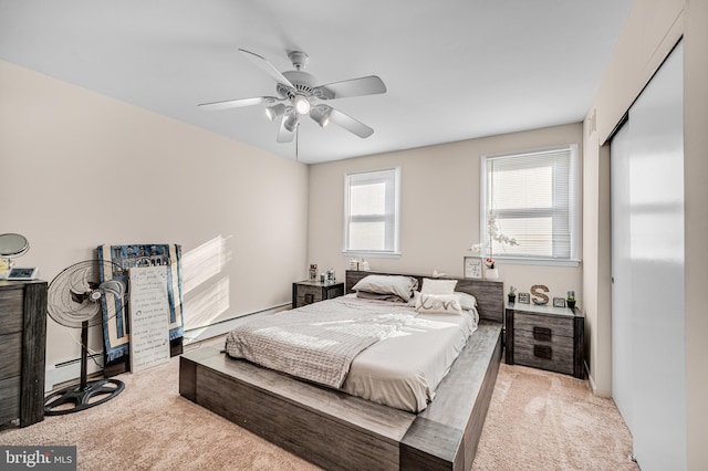 bedroom with light carpet, a closet, ceiling fan, and a baseboard heating unit