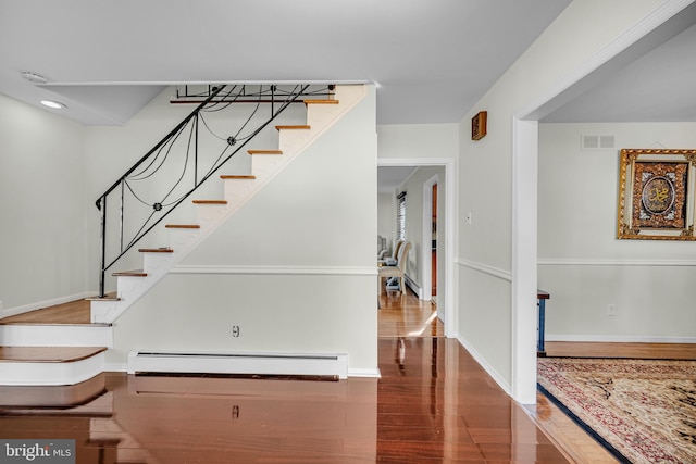 staircase with wood-type flooring and a baseboard heating unit