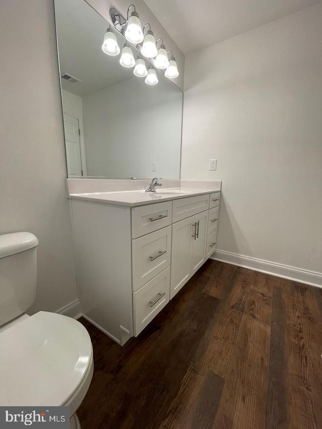 bathroom with toilet, wood finished floors, visible vents, vanity, and baseboards