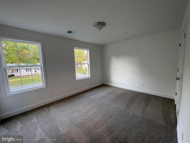 empty room with baseboards, visible vents, and dark colored carpet