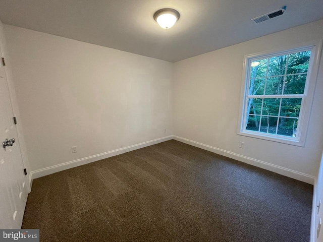 empty room with visible vents, dark carpet, and baseboards