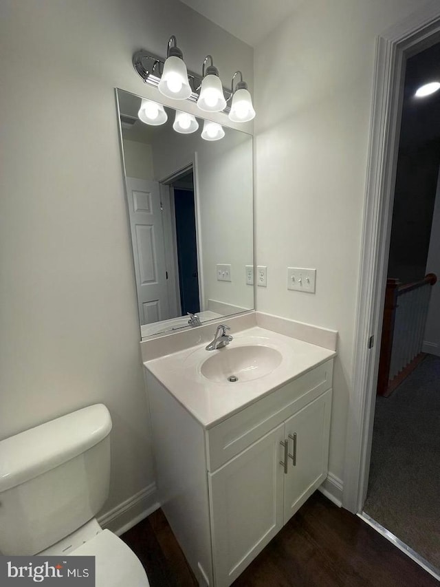 bathroom with toilet, wood finished floors, vanity, and baseboards