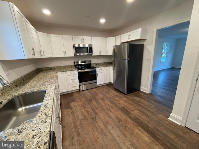 kitchen featuring a sink, white cabinetry, appliances with stainless steel finishes, light stone countertops, and dark wood finished floors