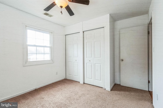 unfurnished bedroom featuring light carpet, ceiling fan, and multiple closets