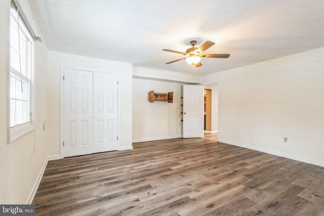 unfurnished bedroom featuring ceiling fan, multiple windows, dark hardwood / wood-style floors, and a closet