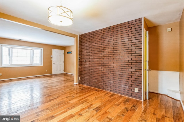 spare room with light hardwood / wood-style floors and brick wall