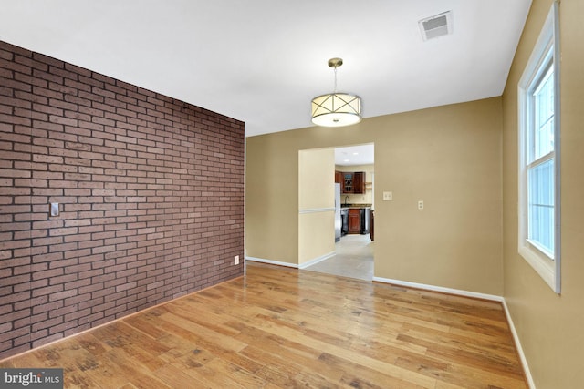 empty room featuring light wood-type flooring, plenty of natural light, and brick wall