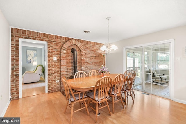 dining area with a chandelier, light hardwood / wood-style flooring, and brick wall